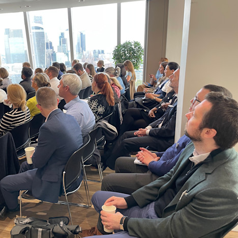 An engaged audience listens, as the City is seen in the background Tile image of An engaged audience listens, as the City is seen in the background