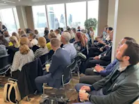 Thumbnail of An engaged audience listens, as the City is seen in the background