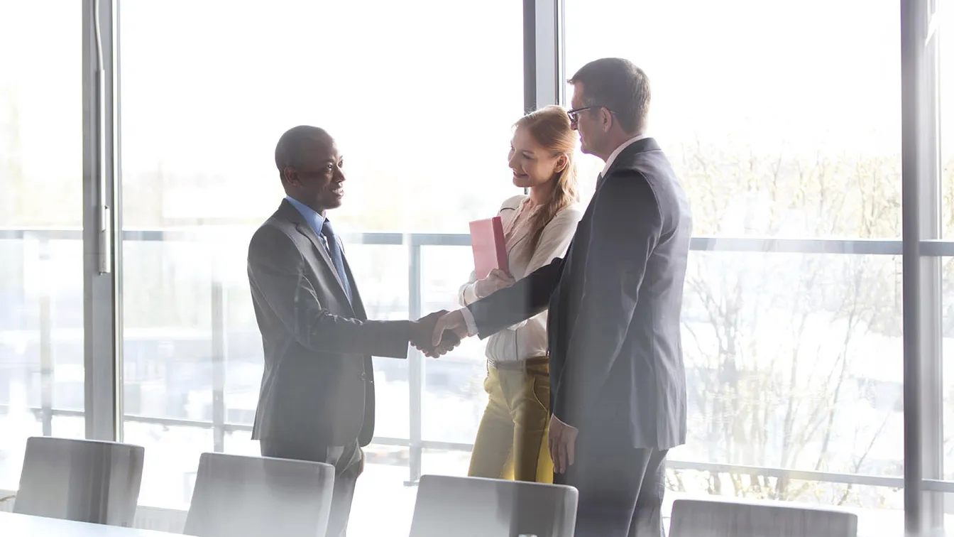 Two businessmen shaking hands as a business woman looks on