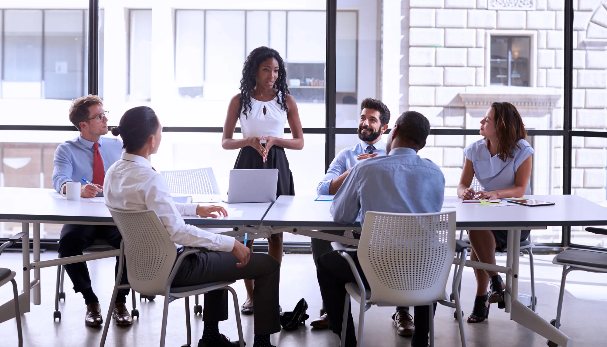 A businesswoman stands to present to her colleagues seated at a table