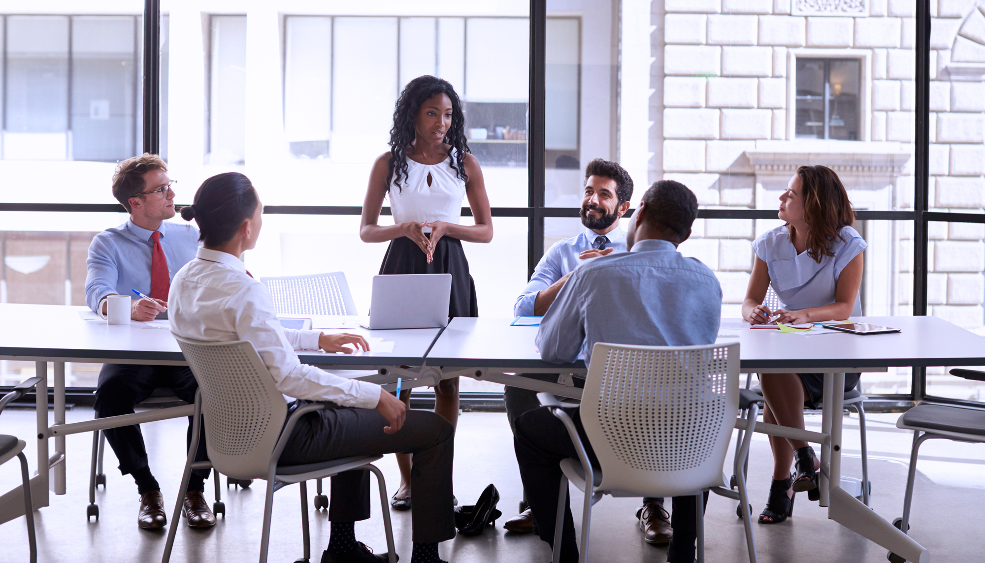 A businesswoman stands to present to her colleagues seated at a table