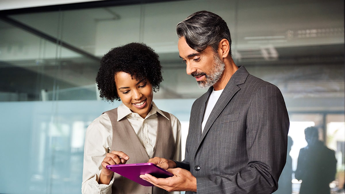 A businessman and a businesswoman look at a purple tablet device together