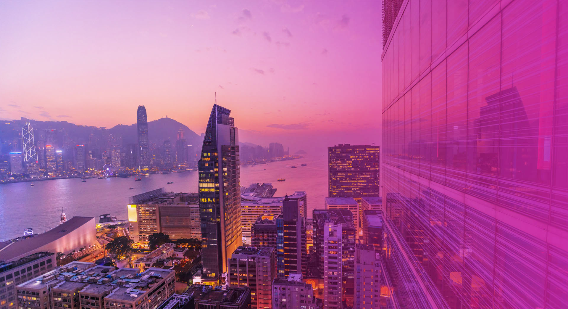 Spectacular aerial view of Victoria Harbor, skyscrapers and Hong Kong skyline at night. Skyline reflected in glass facade of a modern building.
