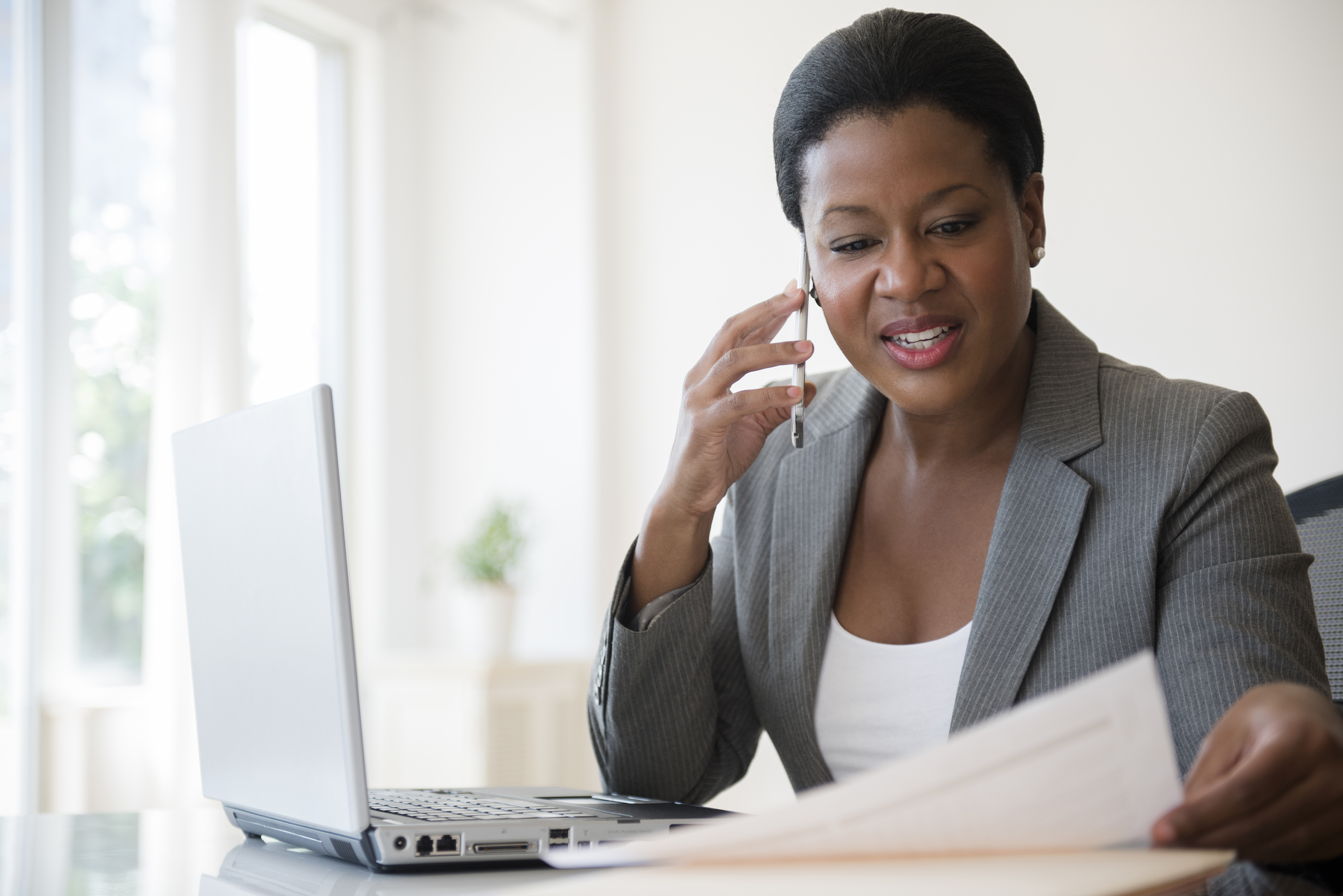 Smiling woman looking down at a contract on her desk while talking on her phone