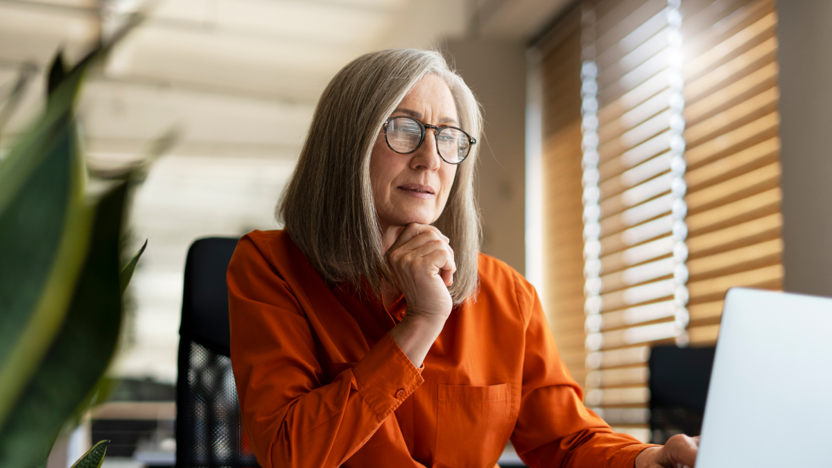 Mature businesswoman with eyeglasses and orange shirt looking at laptop
