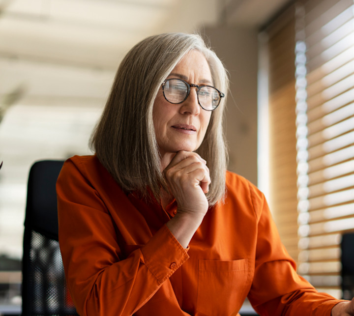 Mature businesswoman with eyeglasses and orange shirt looking at laptop