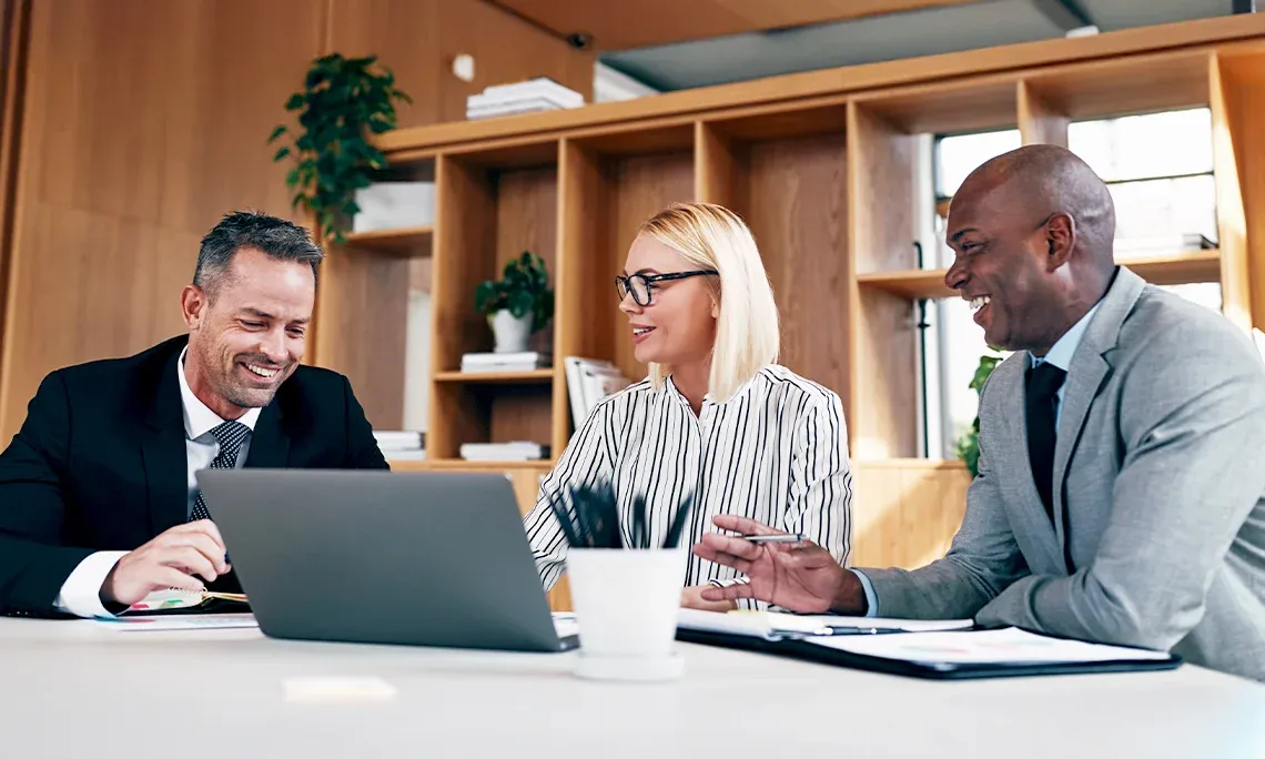 A team of three business people smiling in front of a laptop