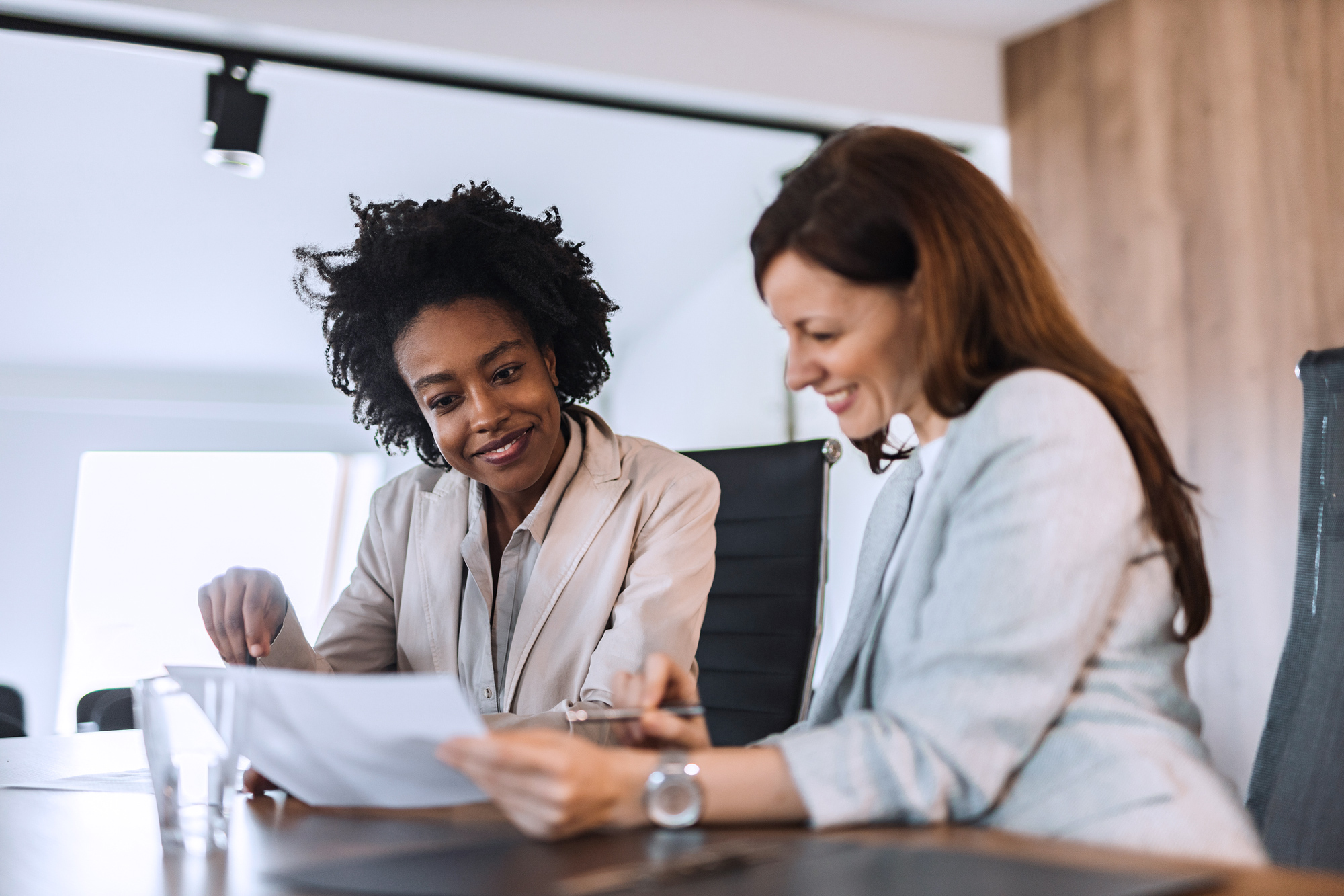 Two businesswomen seated at a table reviewing a document