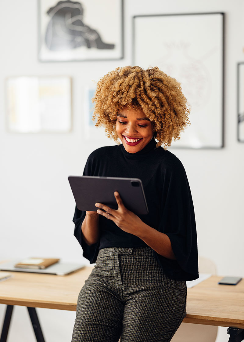 Business woman leaning against a table, reading information on a tablet